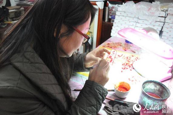 刘亚利的妻子正在为雕刻好的皮影敷彩。